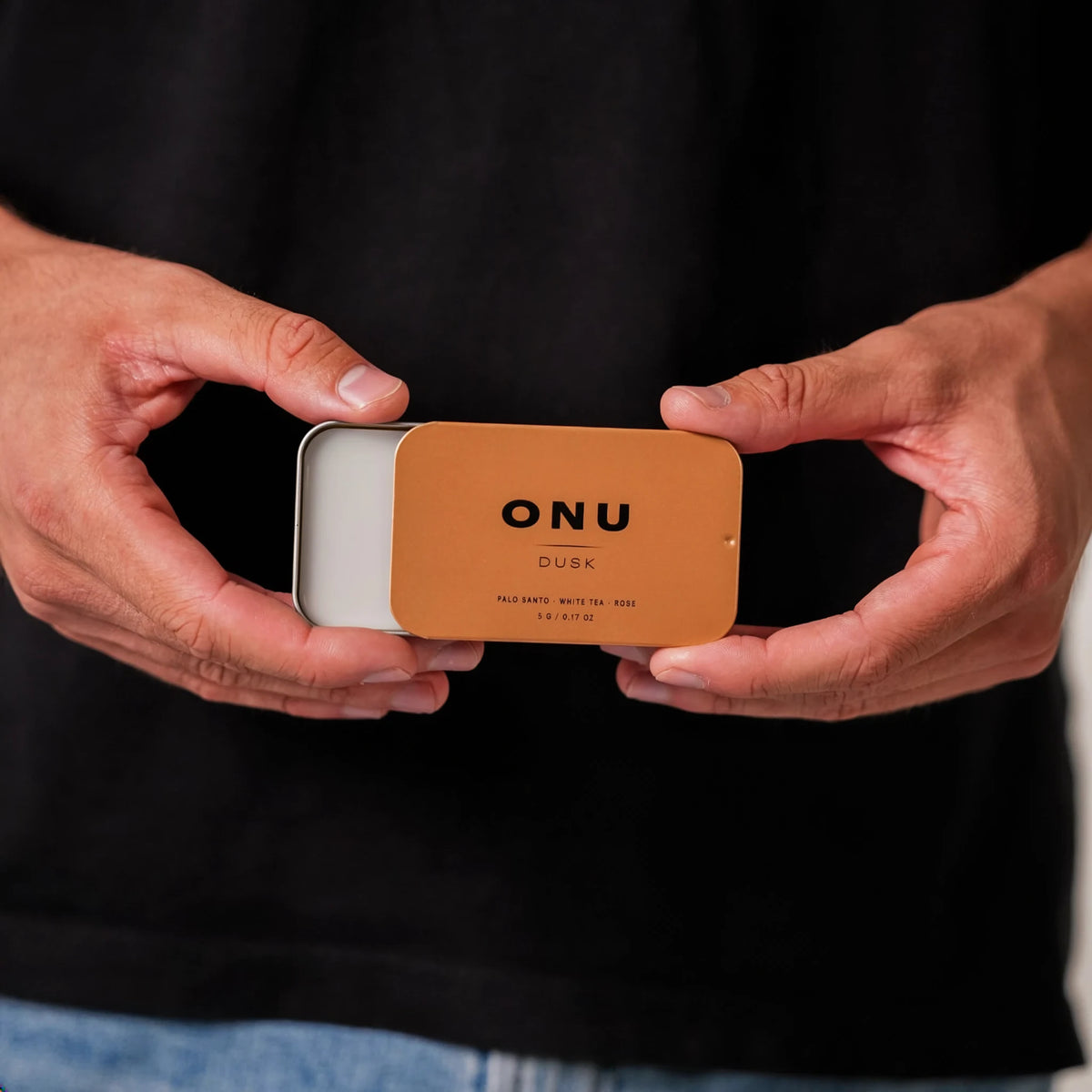 Hands holding an open gold ONU DUSK solid cologne card