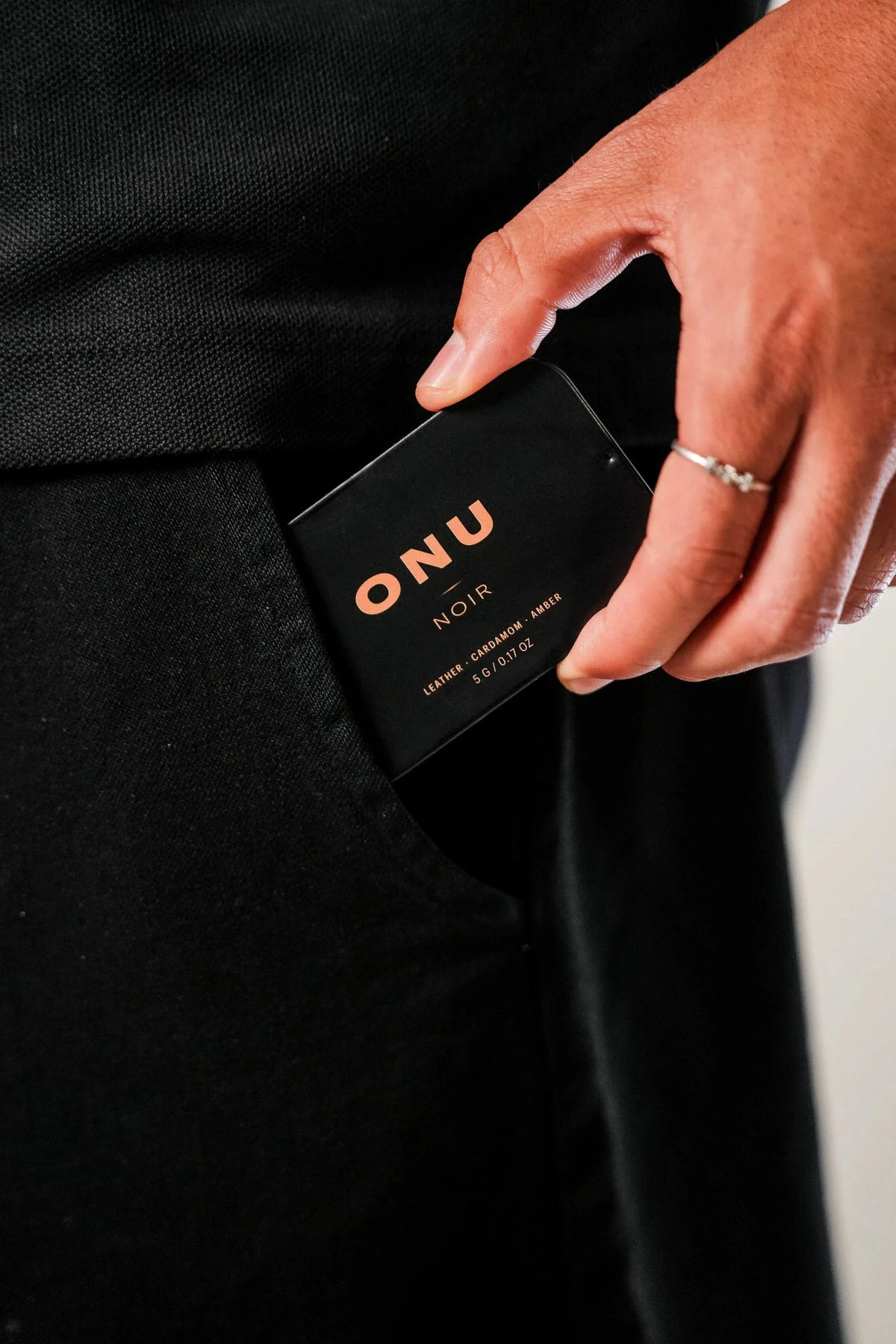 Hand sliding a black ONU NOIR solid cologne card into a black jacket pocket
