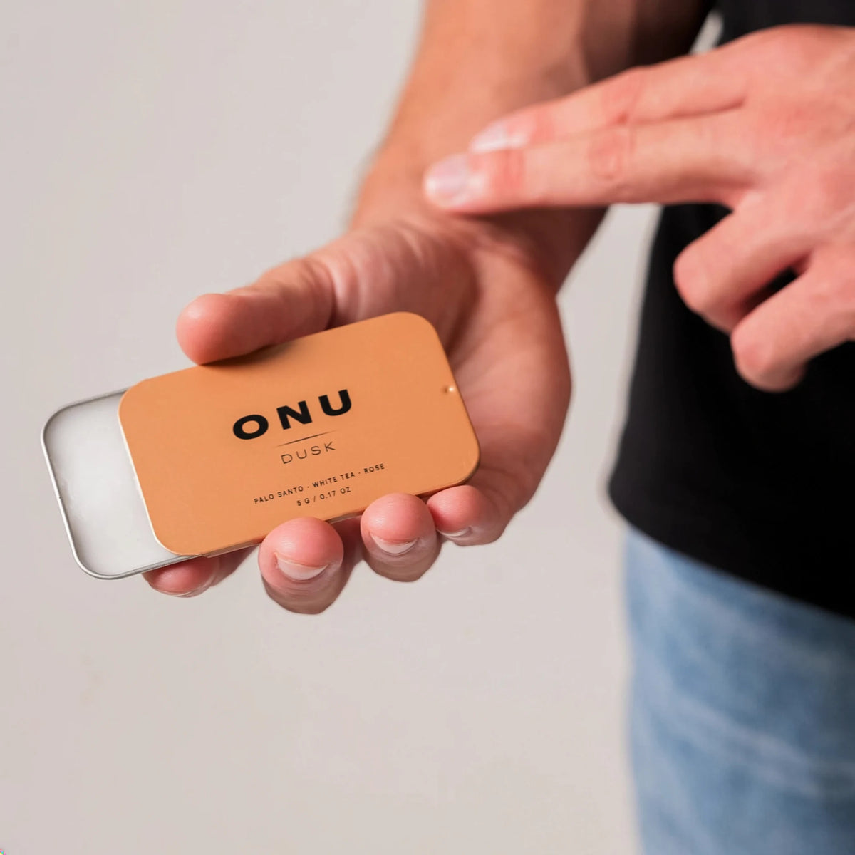 Person applying balm cologne to their wrist from an open gold ONU DUSK card